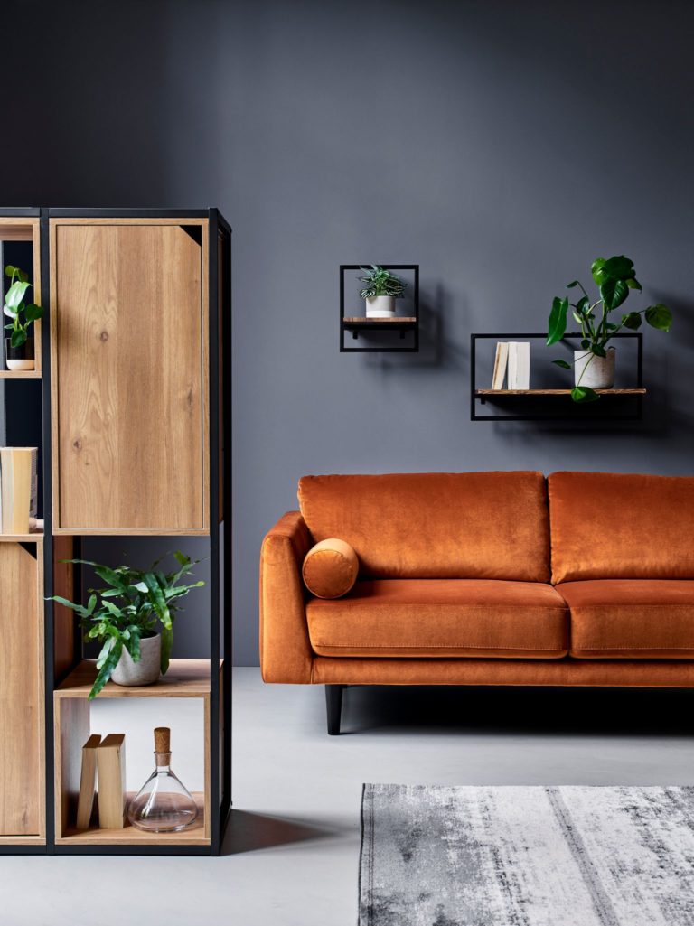 Bright orange mid-century style sofa with floating shelves on the wall behind and large wood and metal shelving unit