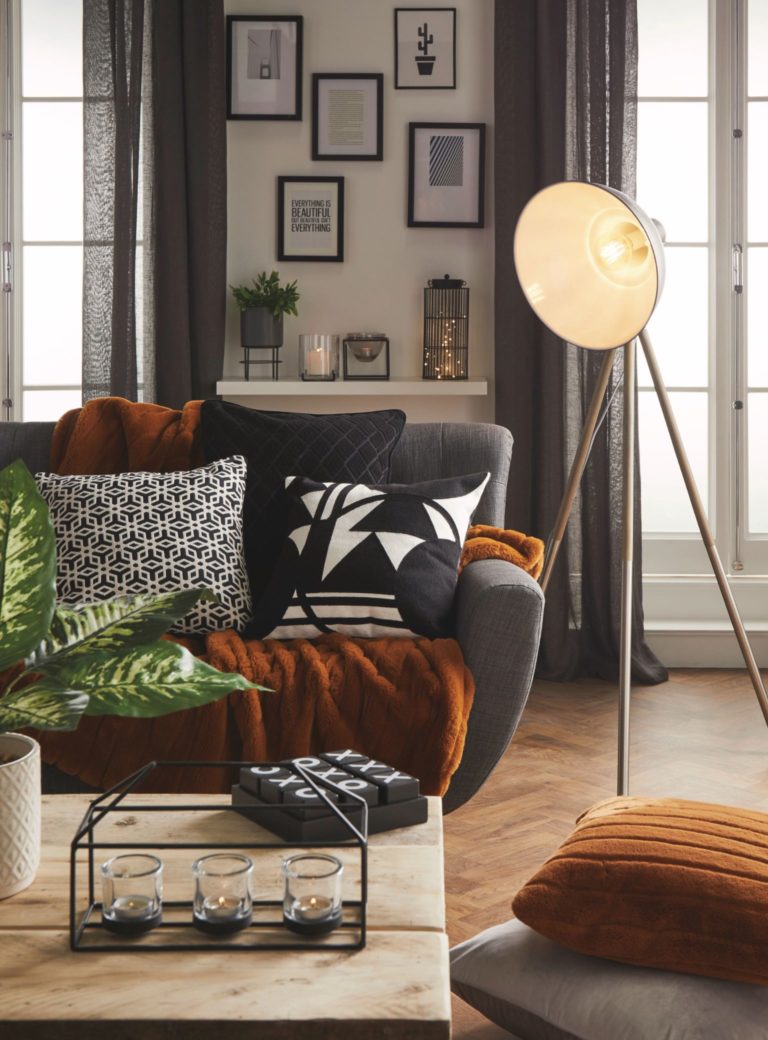 Modern grey sofa with a selection of soft cushions, faux fur throw, Jett Camera Tripod floor lamp and candles. All from Matalan.