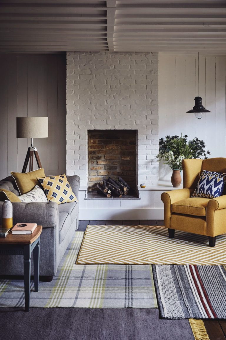 Selection of soft rugs in front of fireplace with grey sofa and yellow armchair