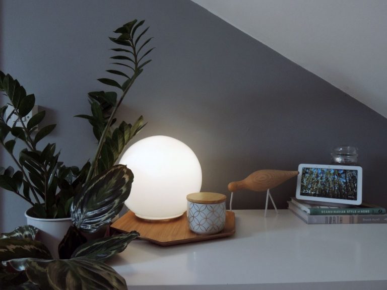 Grey wall with white sideboard in front, warm white ball light on wooden tray with books and a Google Home display.