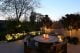 Patio with candles on a round dining table and spotlights lighting up trees