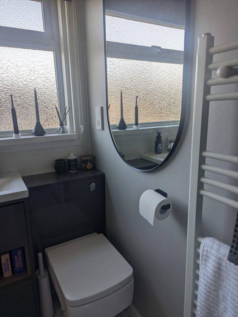Bathroom with grey wall, white radiator and black toilet roll holder and mirror.