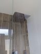 Large square stainless steel shower head on a wall with faux wood tiles.