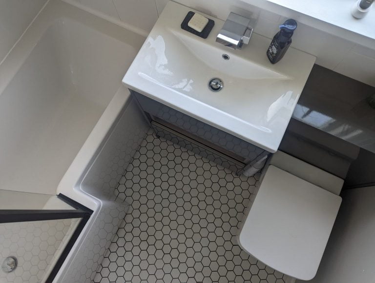 Grey bathroom with white sink and toilet, white hexagon floor tiles and an L-shaped bath.