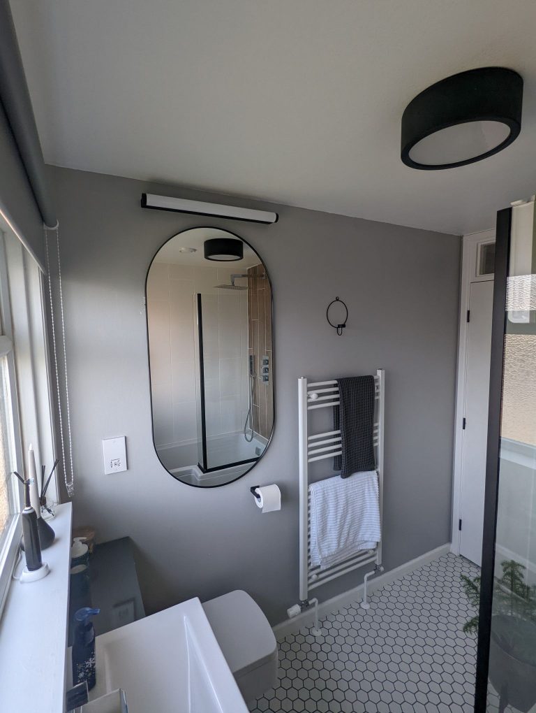 Modern bathroom with hexagon tiles, grey wall and a large oval black framed mirror.
