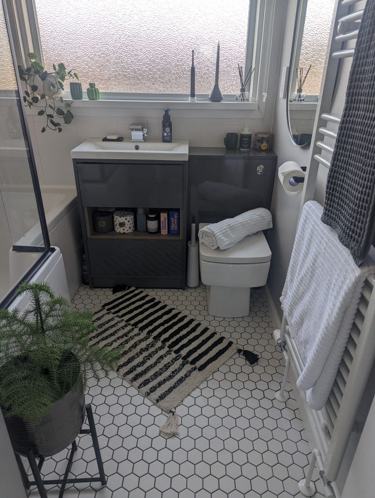 Grey bathroom vanity with faux wood shelf, white hexagon floor tiles and black accents.