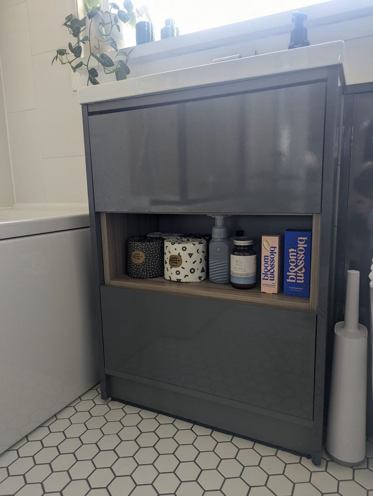 Grey bathroom sink vanity with open wooden shelf.
