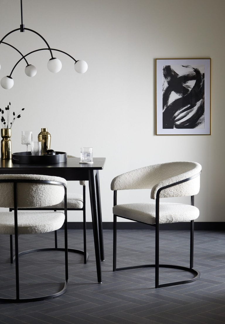 A black metal framed chair with white fluffy fabric, sitting next to a black table which opens up to reveal storage.