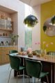 Dining room with a 60s style lamp, etta velvet dining chairs in green with glasses and gold cutlery adorning the walnut table.