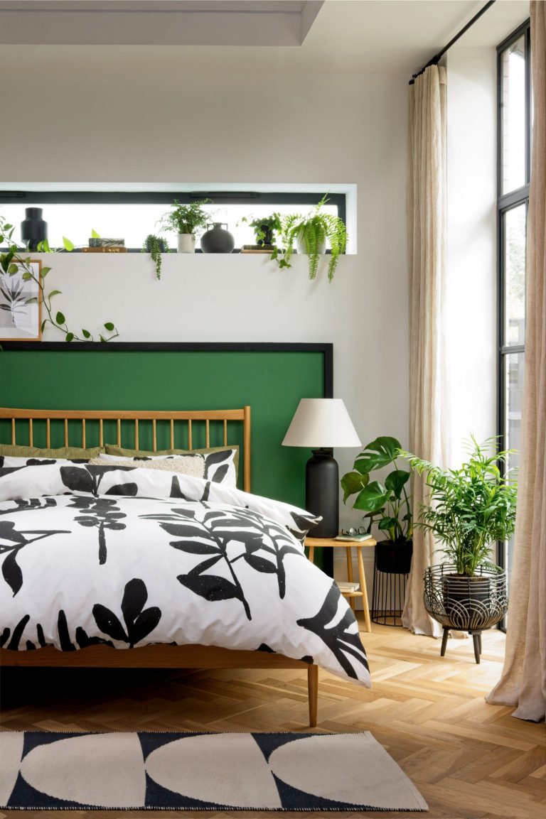 Oak framed bed with a white and black floral print duvet, featuring green plants and a black lamp.