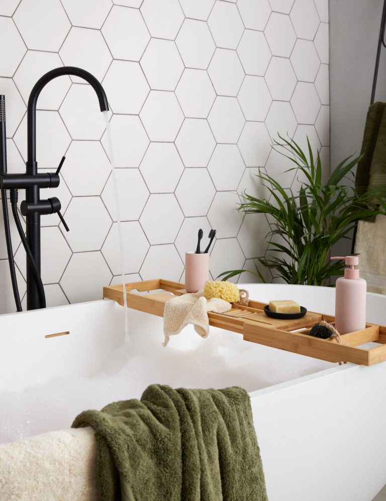 Modern bathroom with hexagon white tiles, black tap and bath rack from Dunelm.