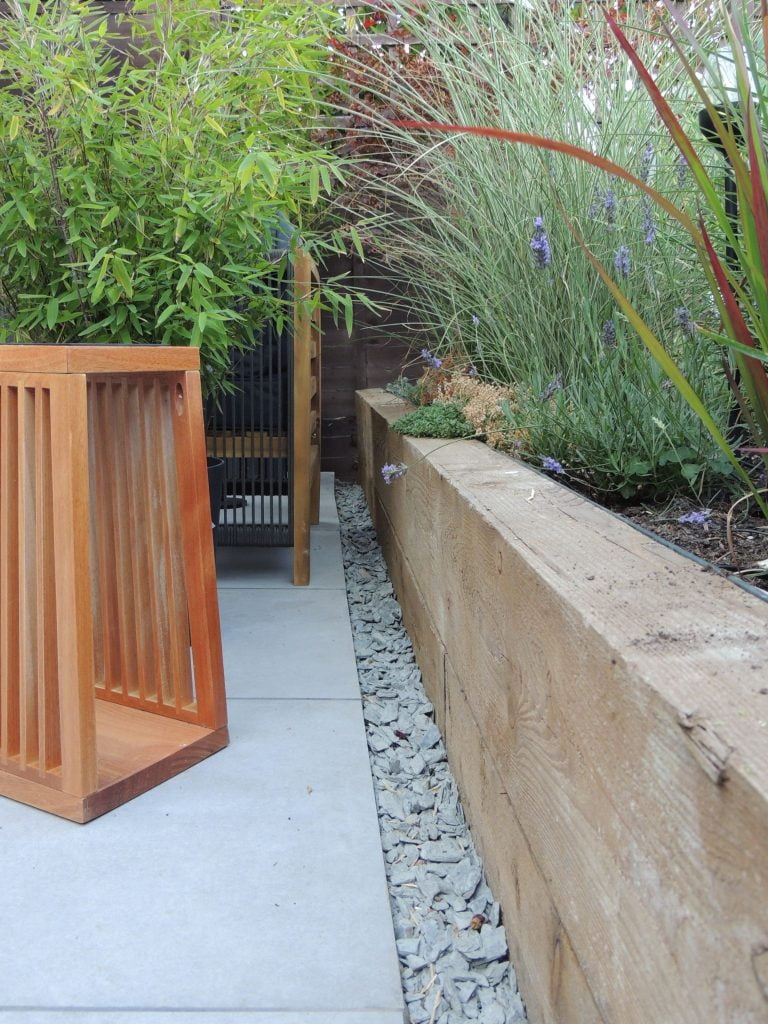 Light grey patio tiles, lined with grey shingles alongside a wooden raised border.