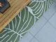 Outdoor wooden coffee table placed upon a printed rug on grey patio tiles.