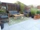 1970s house patio renovation with large grey tiles, modern outdoor sofa set, plants and shade sail.