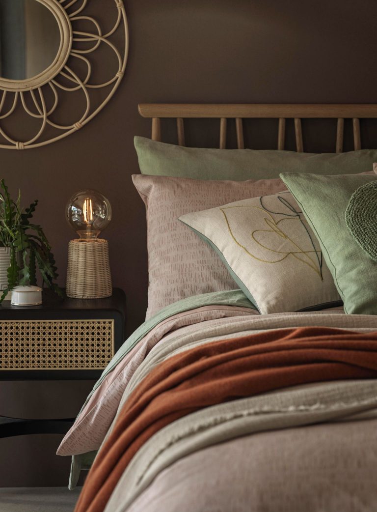 Modern wooden bed frame, with blush bedding, orange throw and rattan storage bedside table from John Lewis.