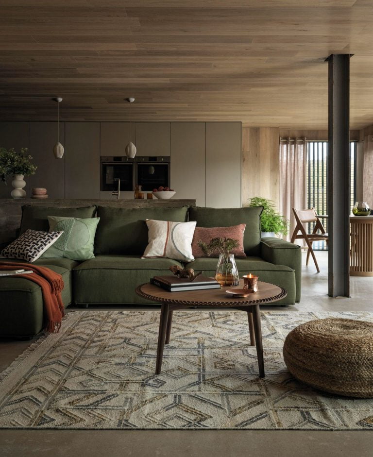 Large low green sofa, dark wood round coffee table and light wood panelled ceiling.