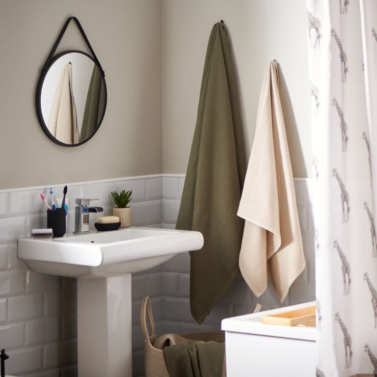 Minimal bathroom with white and cream walls, green towels and a round mirror from Wilko.