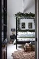 Black four poster bed with white bedding, printed with green trees, green blanket and festive garland.