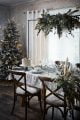 Christmas dinner table with white table cover, hanging floral decorations over the table and a boho style Christmas tree.