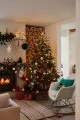 Plain white living room with wall of wood kindling, soft rocking armchair and a large Christmas tree covered in colourful decorations.