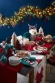 Dark navy blue background with a garland hanging on wall and Christmas table set with colourful decorations.