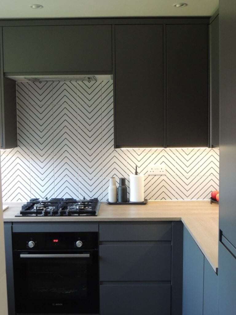 Grey kitchen with black and white splashback tiles.