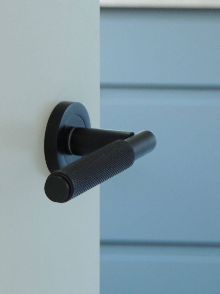 Black knurled metal door handle on a white door.