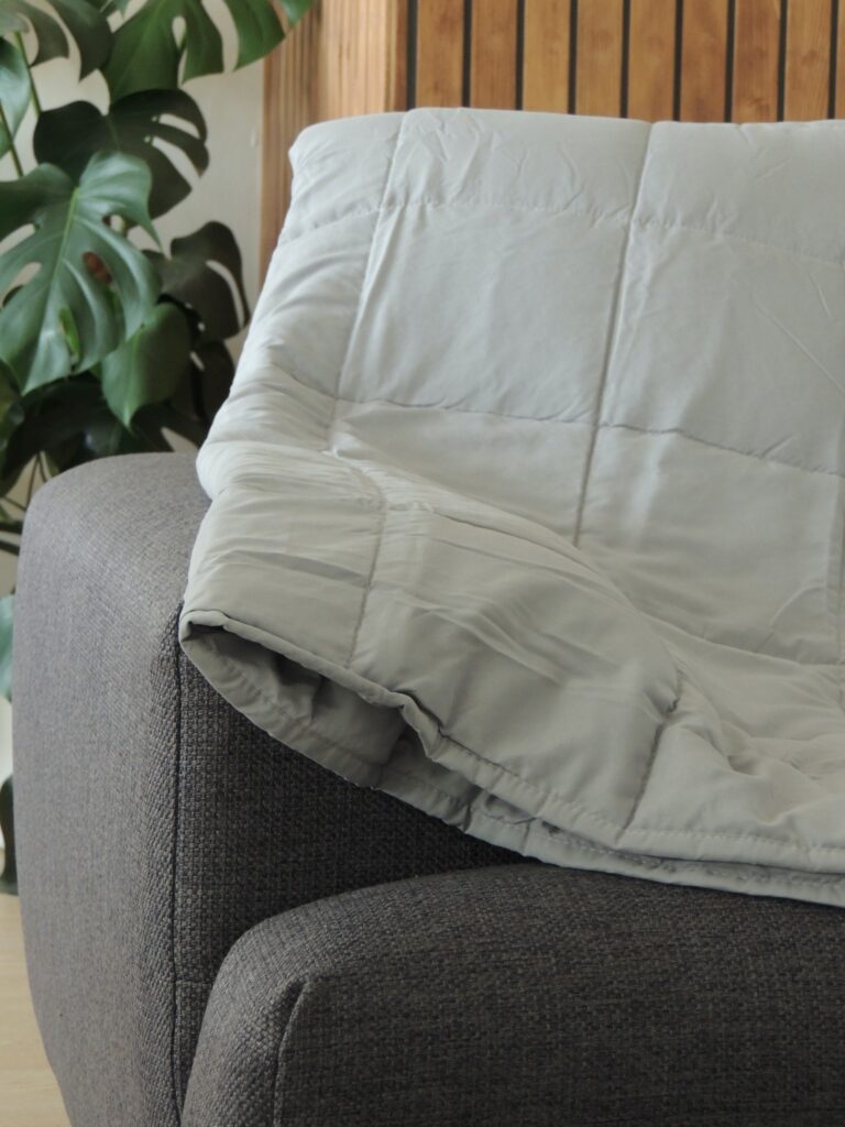 Light grey weighted blanket by Slumberdown, draped over a dark grey sofa.