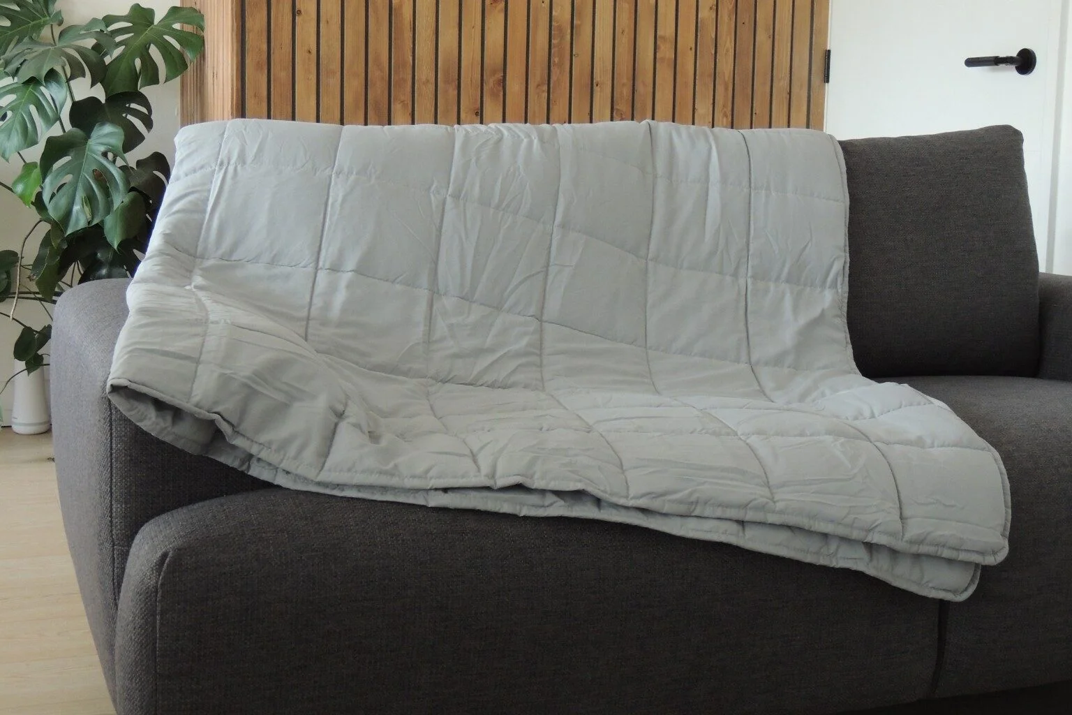 Slumberdown Weighted Blanket draped over a grey sofa with a wooden wall backdrop.