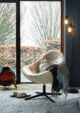 A living room with a white chair sitting in front of a window. The chair is from Dunelm. The chair has a curved back and a cushioned seat. 