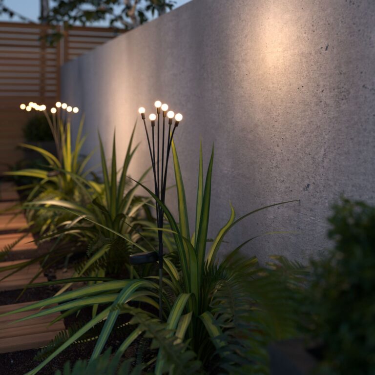 Warm white little glowing lights on top of long black stems, resembling a plant. This lights give of a warm white glowing light and are dotted in-between a border of plants.