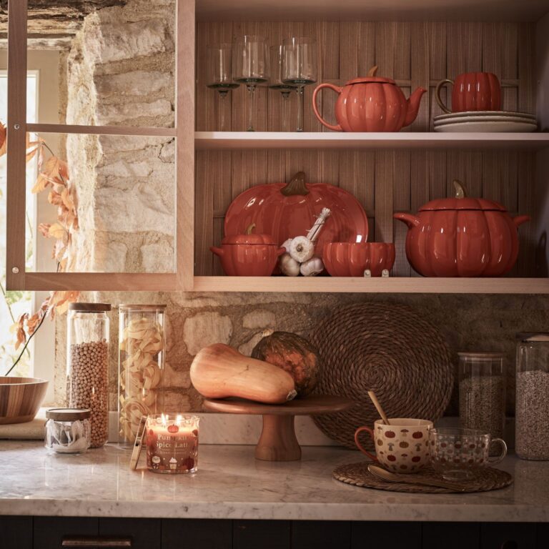 A kitchen filled with pumpkin-shaped dishes. The shelves are lined with pumpkin-shaped bowls, plates, and mugs. There is also a pumpkin-shaped candle on the counter.