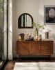 A living room with a sideboard, vases, candles, and a mirror. The sideboard is made of wood and has a mirror on top. There are two vases on the sideboard, one filled with flowers and the other filled with candles. There is also a candleholder on the sideboard.