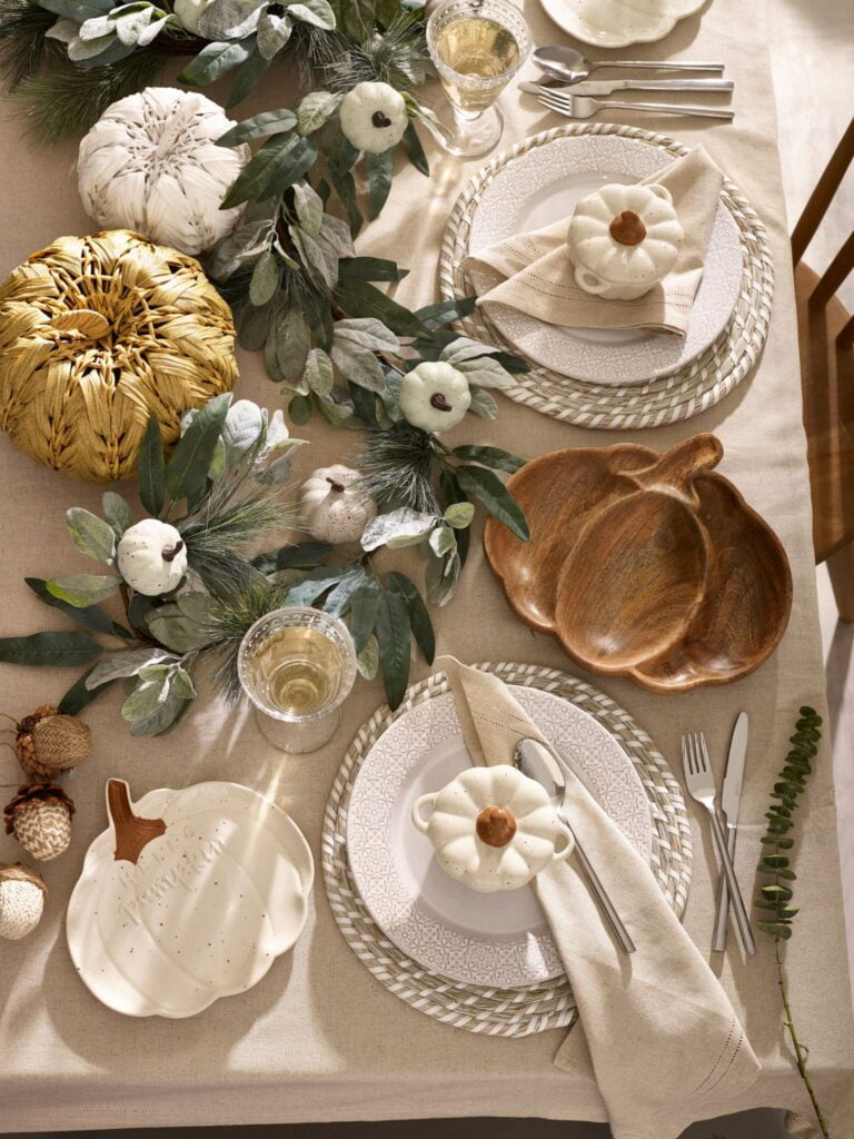 A table set for an autumn dinner party. The table is decorated with pumpkins, leaves, and acorns. The pumpkins are a symbol of fall and the leaves are a symbol of autumn.