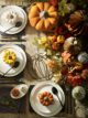Autumn dinner party setup with white plates, small orange pumpkin ramekins, black wire pumpkin shaped trivet and large orange casserole dish.