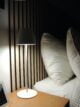 White metal portable tamp lamp on a bedside table with a modern wood slat headboard.