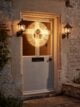 Grey front door with black lanterns either side, on the door is a large round light-up Christmas wreath by Cox and Cox.