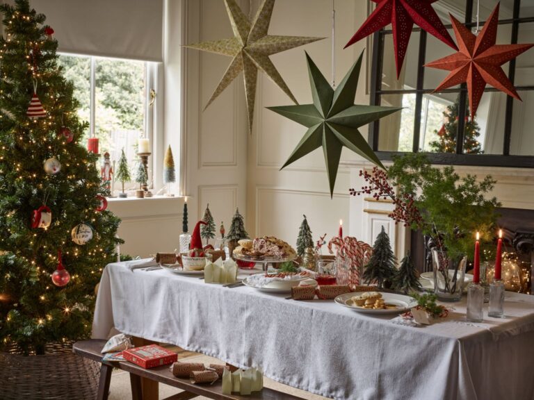Bright and bold Christmas dinner table with hanging paper stars, colourful candles and a white table cloth from Dobbies.