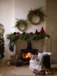 Large fireplace with rattan wreathes above, green garland and pop-up paper Christmas trees by Garden Trading.
