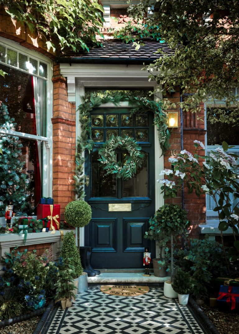 Victorian house with tile footpath, dark black front door with a large green wreath and a garland surrounding it.