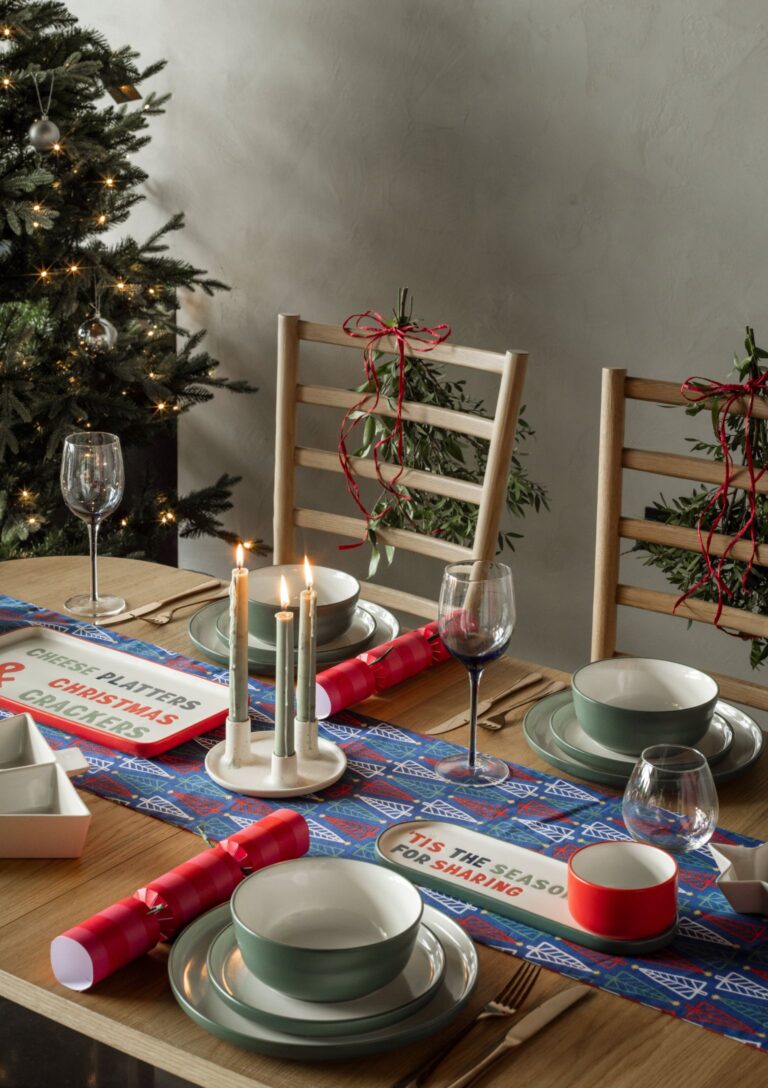 Colourful Christmas dinner table with a Christmas tree table runner, green dinner plates and red crackers from Habitat.