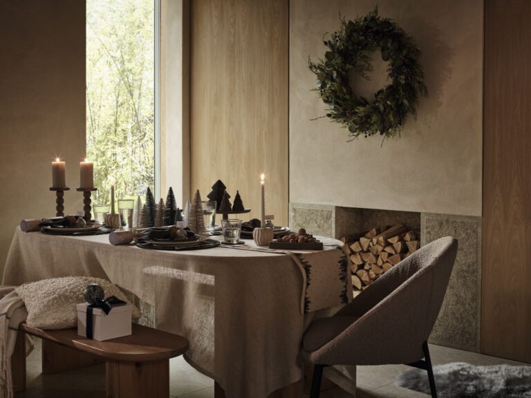 Neutral Christmas dinner table with a fabric table cloth, wooden trees and candles from Marks and Spencer.