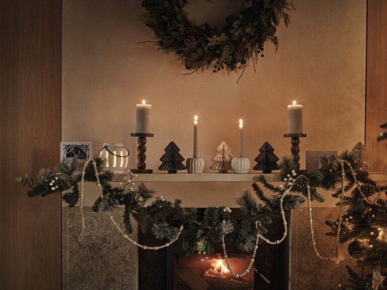 Mantelpiece with large pillar candles and a greenery garland draped along the shelf by Marks and Spencer.
