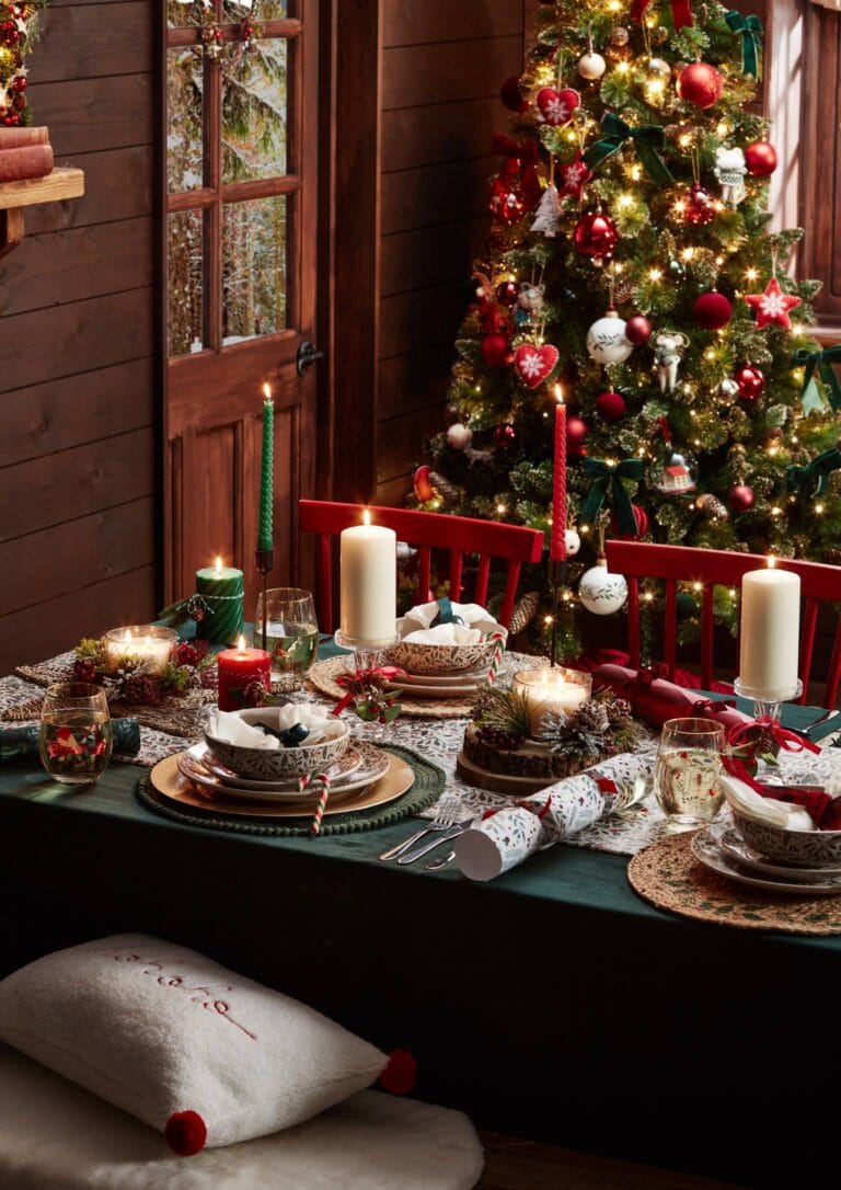 Dark green Christmas dinner table, filled with dinner plates, candles, crackers and cutlery.