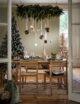 Large hanging faux tree garland over a dining table with hanging christmas presents. This is a modern wooden dining table, with a Christmas tree in the corner, ready for a Christmas dinner.