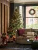 Large bay window with a sofa sat inside, hanging Christmas wreath and a large Christmas tree. The Christmas style is very traditional with reds, golds and greens.