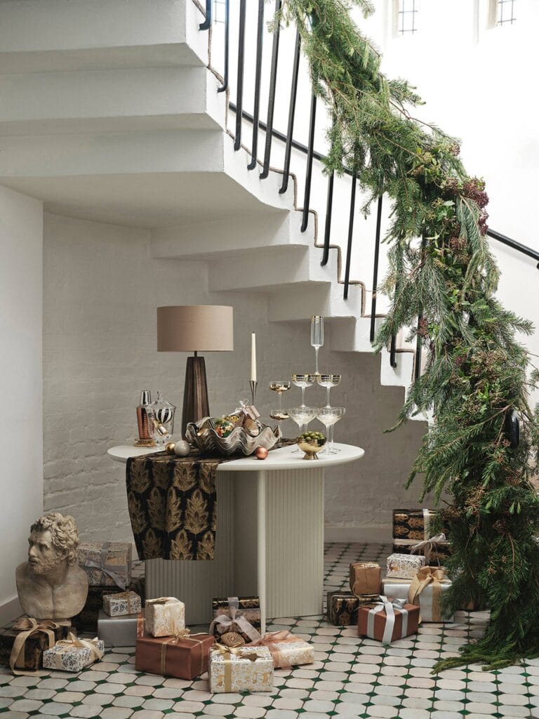 A grand staircase draped in greenery, a table set with champagne flutes, and a pile of wrapped presents – it's the perfect spot for a holiday gathering.
