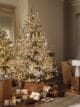 White snowy tree, lit with warm Christmas lights, surrounded by a bunch of presents.